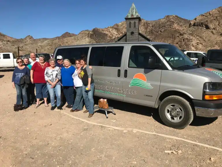 a group of people standing in front of a Desert Wonder Tours passenger van